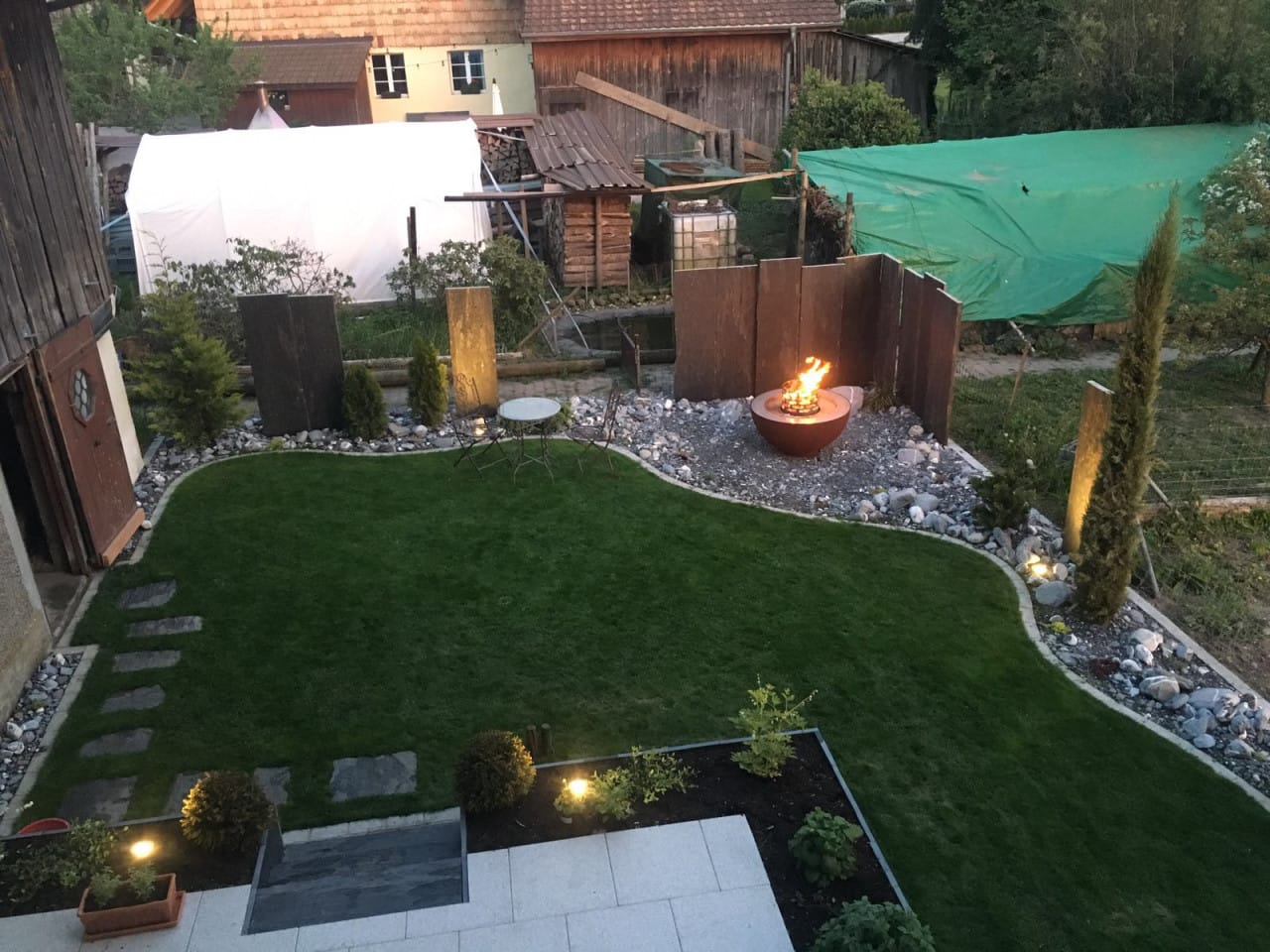 Fertiger Garten mit Rasen, Steinrabatten und Feuerschale am Abend